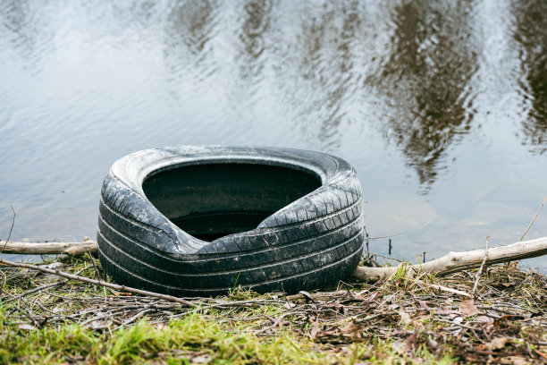 一辆旧汽车轮胎躺在河岸上，环境受到污染图片下载