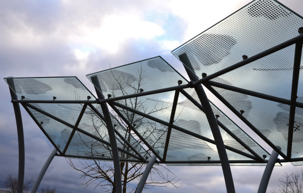 自行车车棚与玻璃屋顶与点印。由弯曲的灰色管构造成弧线。城市公园里金属手柄上的钢化夹胶玻璃。图片下载