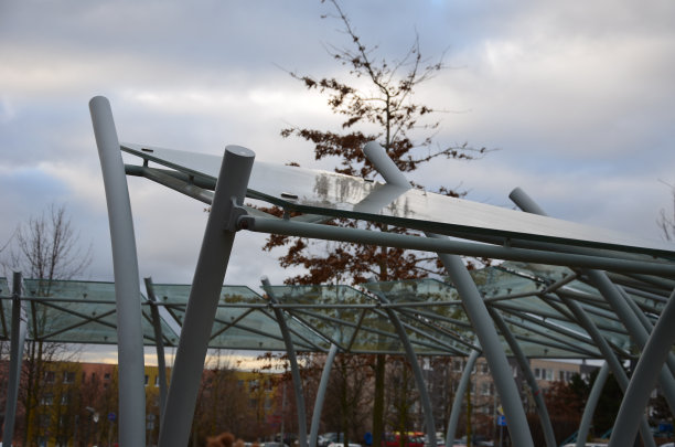 自行车车棚与玻璃屋顶与点印。由弯曲的灰色管构造成弧线。城市公园里金属手柄上的钢化夹胶玻璃。图片下载