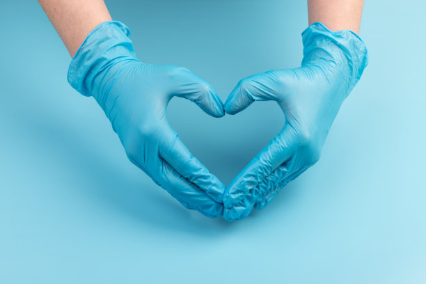 医生的手在医疗手套的形状在蓝色背景与复制空间的心脏。图片下载