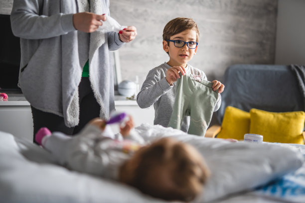 白人男孩，小孩和他的母亲年轻的女人照顾婴儿弟弟或妹妹，换衣服，穿衣服，躺在家里的床上，真实的人，家庭和纽带的概念图片下载