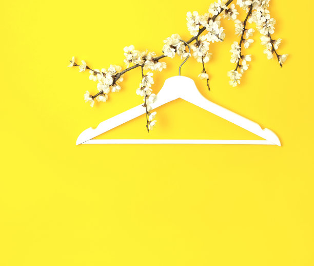 白色的木衣架悬挂在黄色背景的春天开花的树枝上。春季打折概念店购物空衣架。创意时尚美旗。平躺顶视图复制空间。图片下载