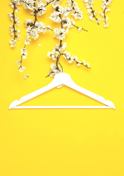 白色的木衣架悬挂在黄色背景的春天开花的树枝上。春季打折概念店购物空衣架。创意时尚美旗。平躺顶视图复制空间。图片下载