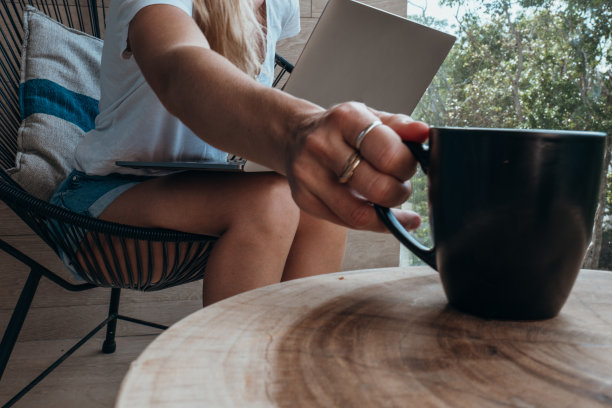 一个年轻女人在阳台上用电脑工作，喝着饮料图片下载