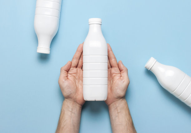 白色塑料瓶容器乳制品在男性手中蓝色背景俯视图平躺。塑料开菲尔酸奶奶瓶。包装模板模型。设计的布局图片下载