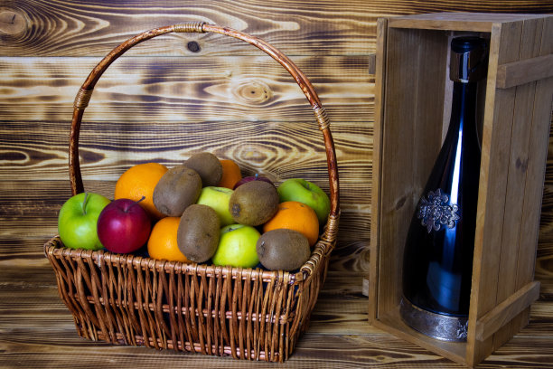 一个柳条篮子和明亮的水果和一瓶葡萄酒在礼物木盒。图片下载