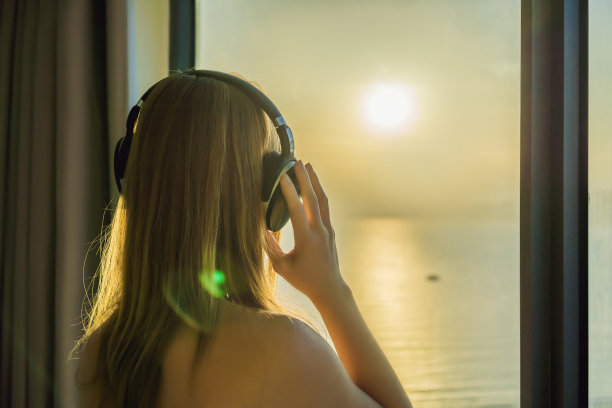 清晨，一名女子坐在一扇海景窗边，用无线耳机听音乐图片下载