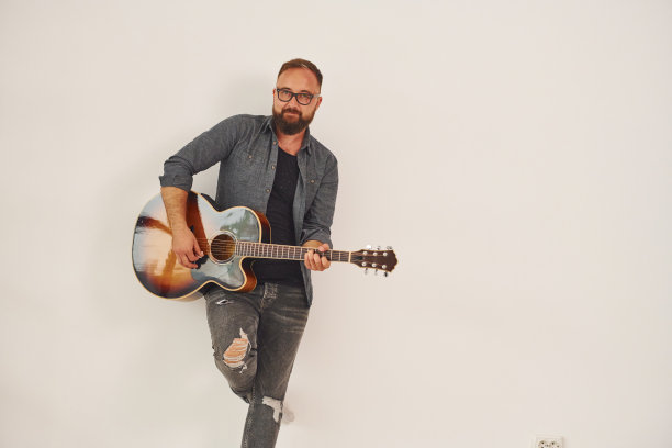 站在演播室里。一个穿着便服，拿着原声吉他的男人在室内图片下载