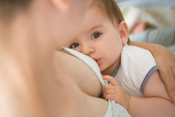 年轻的白人母亲和婴儿在内部位置。妈妈在白色的卧室里给孩子喂奶。幼儿园内部。家人在家里图片下载