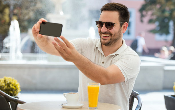 在线视频交流。年轻人坐在咖啡馆里，用智能手机和朋友视频通话。生活方式、技术图片下载