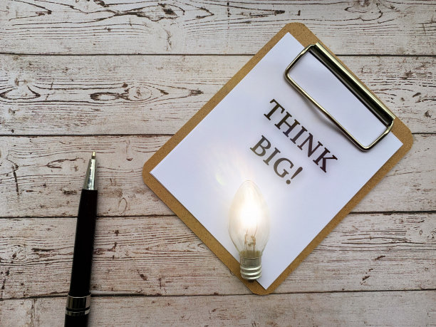 俯视图的文本在记事本-想大。以灯泡、钢笔和木制书桌为背景。经营理念。图片下载