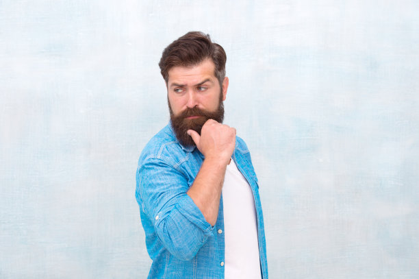 大胡子男人新潮嬉皮士风格。理发沙龙。打扮的男子气概。留着胡子的潮人会穿牛仔衬衫。男性美容的概念。残酷英俊的潮人在灰色的墙壁背景图片下载