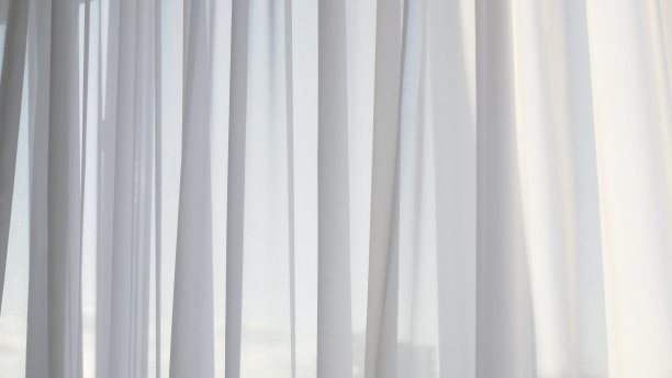 窗户上挂着白色的薄纱窗帘。薄纱窗帘增加了家庭的舒适和舒适。温柔的阳光透过薄纱窗帘。薄纱项链轻轻摆动图片下载