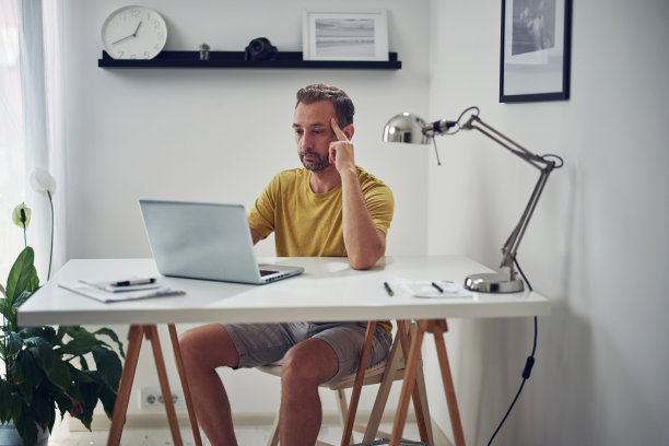 成年白人男子在家用笔记本电脑工作。图片下载