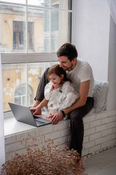 父亲和女儿坐在靠近窗户的白色木质窗台上玩笔记本电脑图片下载