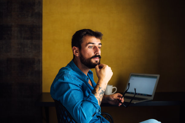 一个年轻的、沉思的男人正坐在椅子上，揉着下巴，休息了几分钟。图片下载