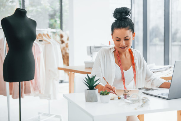 坐在桌子旁边。女裁缝在她的办公室里穿着不同的衣服图片下载