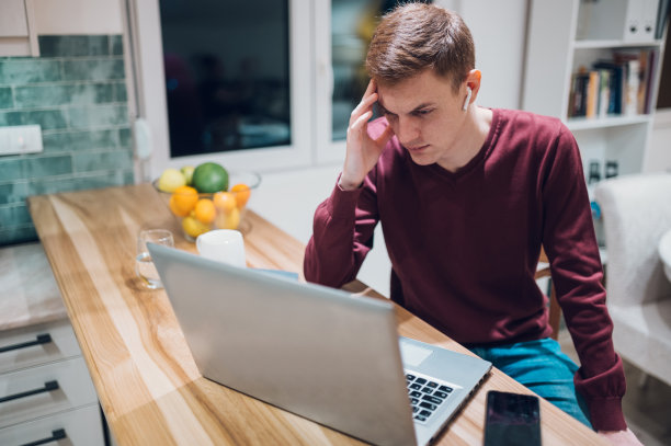 红发男子在家使用笔记本电脑时头疼。图片下载