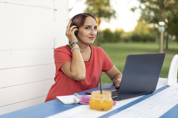 在公园网上工作的女商人。自由职业者使用技术在任何地方工作。一名女子在户外用耳机和笔记本电脑与顾客交谈。图片下载