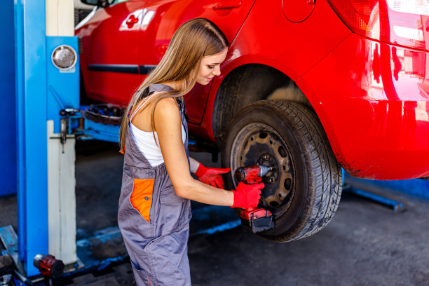 一个年轻的女汽车修理工在一家汽车服务公司给汽车换轮胎。图片下载
