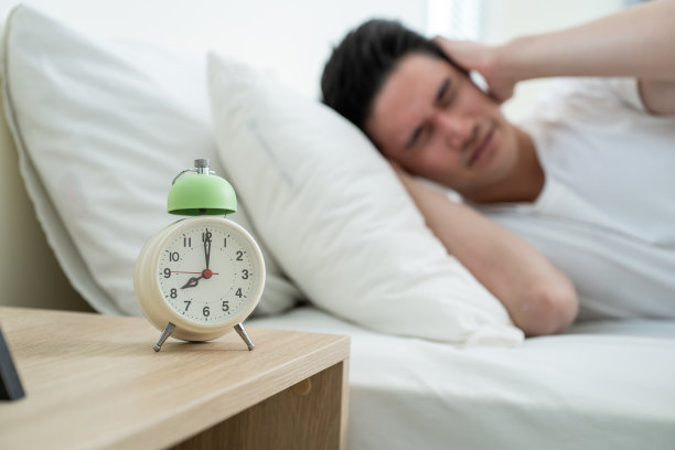亚洲有吸引力的年轻男子睡觉时，闹钟在早上响。帅男觉得懒，累了躺在舒适的床上，在卧室里无视噪音，继续睡觉不想醒来。图片下载