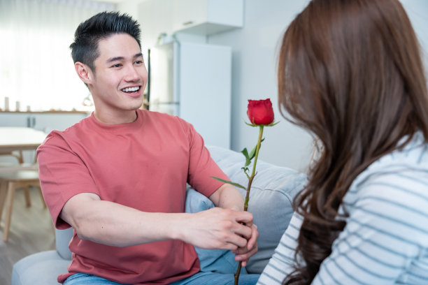 亚洲青年惊喜送玫瑰给美丽的女友。迷人浪漫的新婚男女花时间在房子里一起庆祝周年纪念日和情人节。图片下载