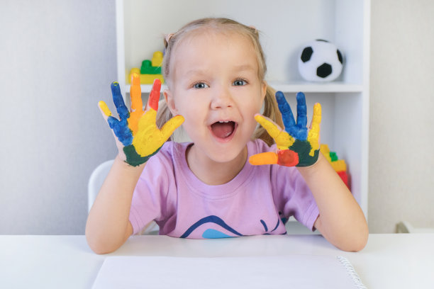 美丽的金发小女孩，她的手上涂着彩色颜料图片下载