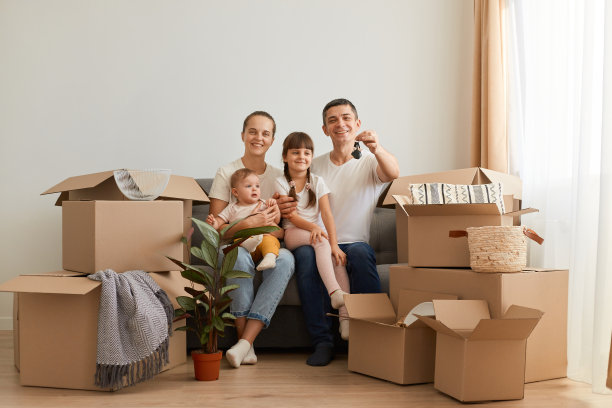这张照片拍摄的是一对年轻的白人夫妇和孩子们坐在地板上，周围都是纸箱，他们搬到一个新公寓，穿着白色的t恤，男人展示着他们新家的钥匙。图片下载