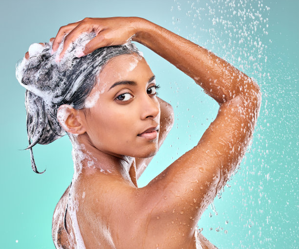 一个美丽的年轻女子在蓝色的背景下享受肥皂淋浴图片下载