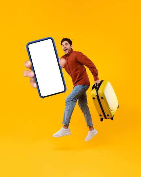 男性游客跳着拿着巨大的智能手机和手提箱，黄色背景图片下载