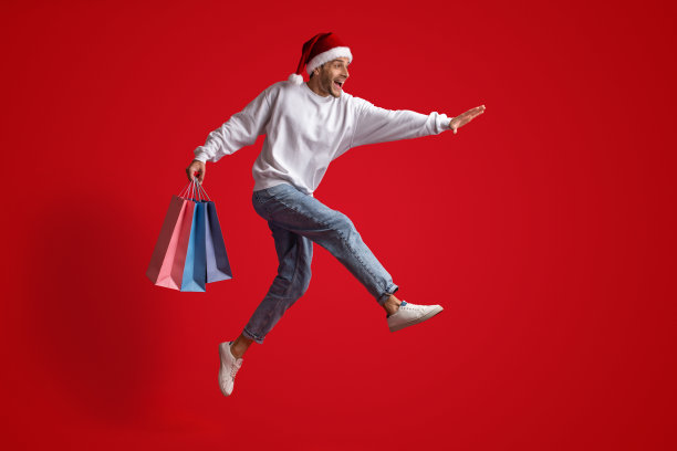 季节性销售。戴着圣诞帽的快乐男人拿着购物袋奔跑图片下载