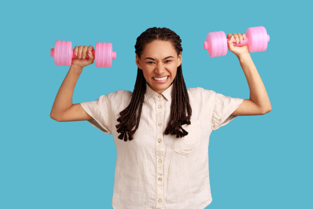 手里拿着粉色哑铃的女子，微笑着看着镜头，锻炼肌肉。图片下载