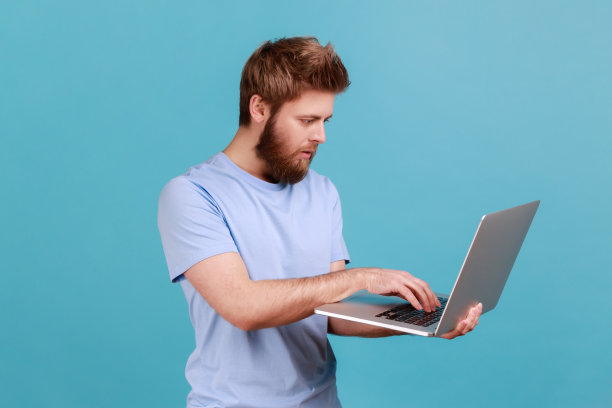 穿着蓝色t恤的男人手里拿着无线电脑，在笔记本电脑上工作，编辑，截稿。图片下载