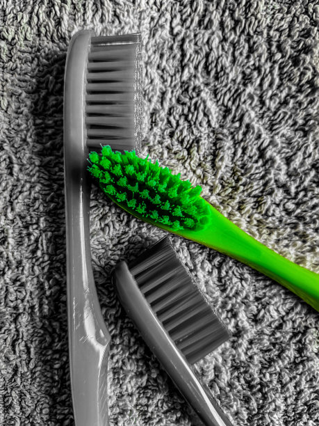 三支牙刷躺在毛巾上。除了一只牙刷是亮绿色外，照片其余部分都是黑白的。图片下载