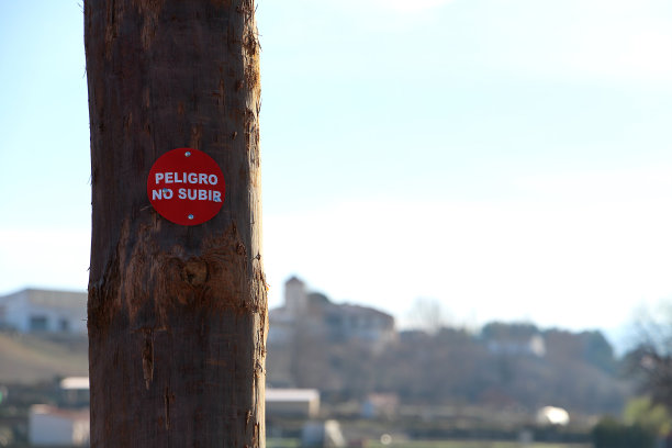 一根木桩或木棒的近距离照片，上面有一块红色的板，上面有白色的字母，用西班牙语写着“危险，不要攀爬”图片下载