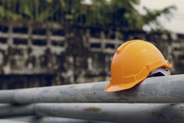 橙色工人安全头盔保护建筑施工工人或工业工厂。戴在铁柱上的安全帽。概念蓝领图片下载