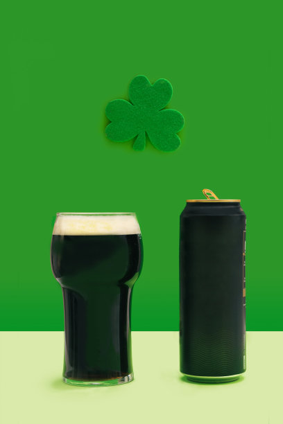 一品脱黑啤酒杯和啤酒罐孤零零地站在绿色的三叶草上面。幸运酒吧最小概念。图片下载