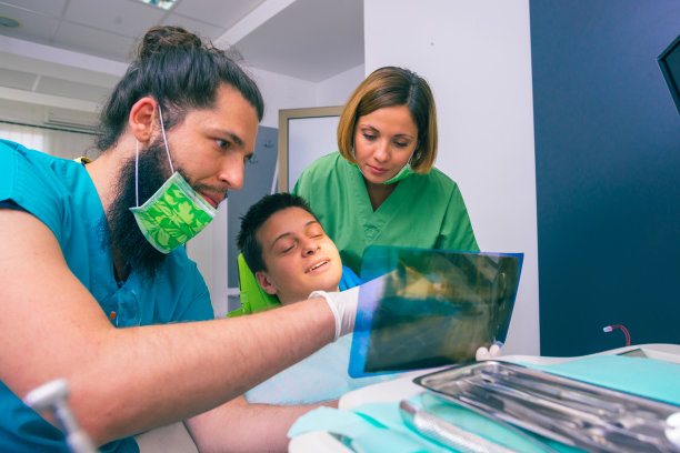 男女牙医在牙科诊所给一个小男孩病人看他的牙齿x光图像。图片下载