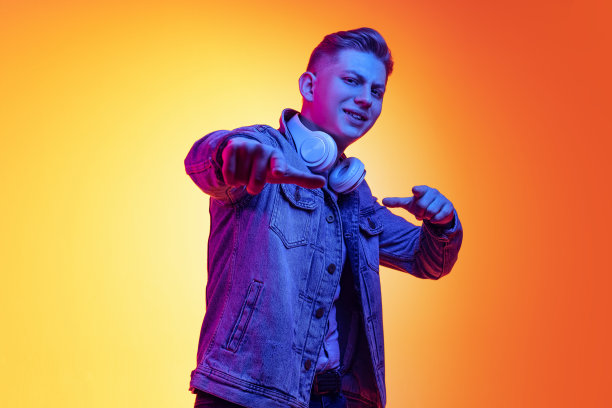 情绪化的年轻英俊的男子在休闲的青年风格的衣服孤立在橙色的背景霓虹灯，滤镜。情感、美、时尚的概念图片下载