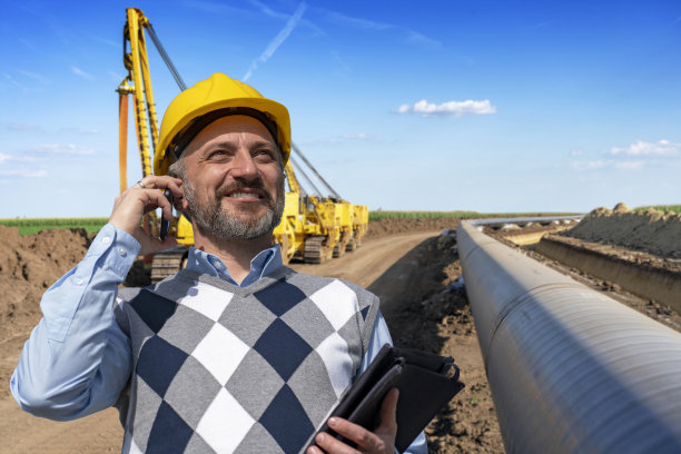 燃气管道施工现场微笑的工头手持手机的照片图片下载