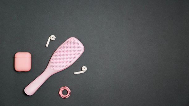 一个时尚的浅粉色女孩的工具包发刷与头发戒指，和扬声器与充电盒在深灰色背景平躺风格的粉红色覆盖图片下载