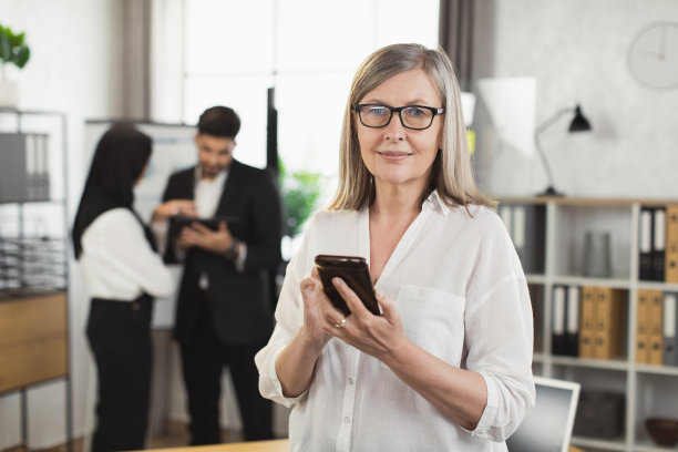 一位灰白头发的女商人在办公室使用手机图片下载