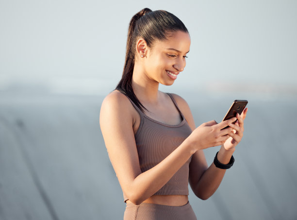 这张照片拍摄的是一位年轻的运动女性在户外运动时使用手机图片下载