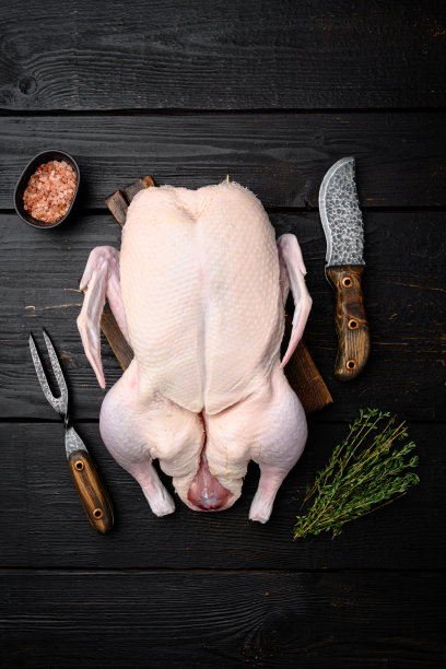 整只新鲜生鸭准备与香草烹饪，黑色木制桌子背景，俯视图平躺图片下载