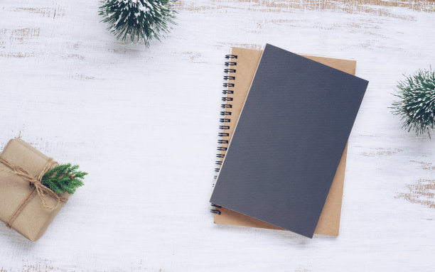 模型空白黑色书封面与圣诞礼物盒和圣诞树模型装饰在白色木制桌子背景。平躺，顶视图与复制空间图片下载