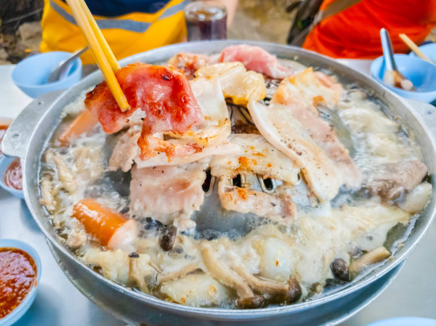 用木筷子夹着烤肉，泰式烤肉在热锅上烧烤，在热炉子上烤猪肉，一个假日家庭在餐馆吃饭。智能手机的照片图片下载