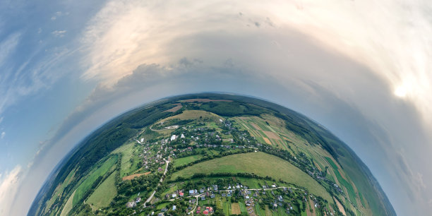 在晴朗的夏日，从高空俯瞰小星球地球，小村庄的房屋和远处绿色耕种的农田，庄稼正在生长图片下载