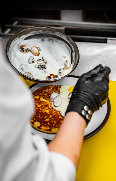 厨师双手戴着手套在厨房里用蘑菇酱、培根和鸡蛋煎薄饼图片下载