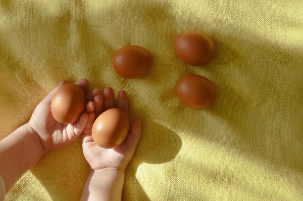 复活节快乐。节日装饰。棕色的鸡蛋在一个孩子的手中，黄色的背景。图片下载