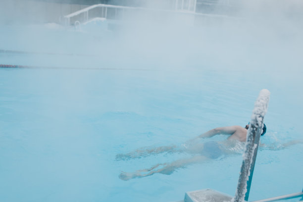 健康的游泳运动员男性训练游泳在开放的冬季游泳池与雾。地热户外spa概念，图片下载